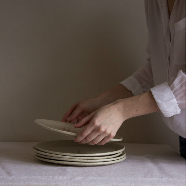 Several clay plates, coated with ashes from local pines. Model in a white cotton blouse. Handmade in Mallorca. 